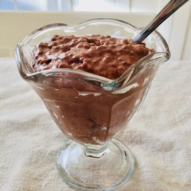 Glass dish filled with chocolate pudding with a spoon in it.