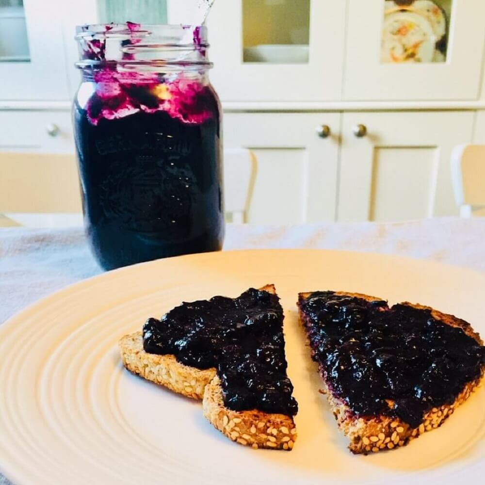 Blueberry jam spread on some toast with a glass jar of jam in the background.