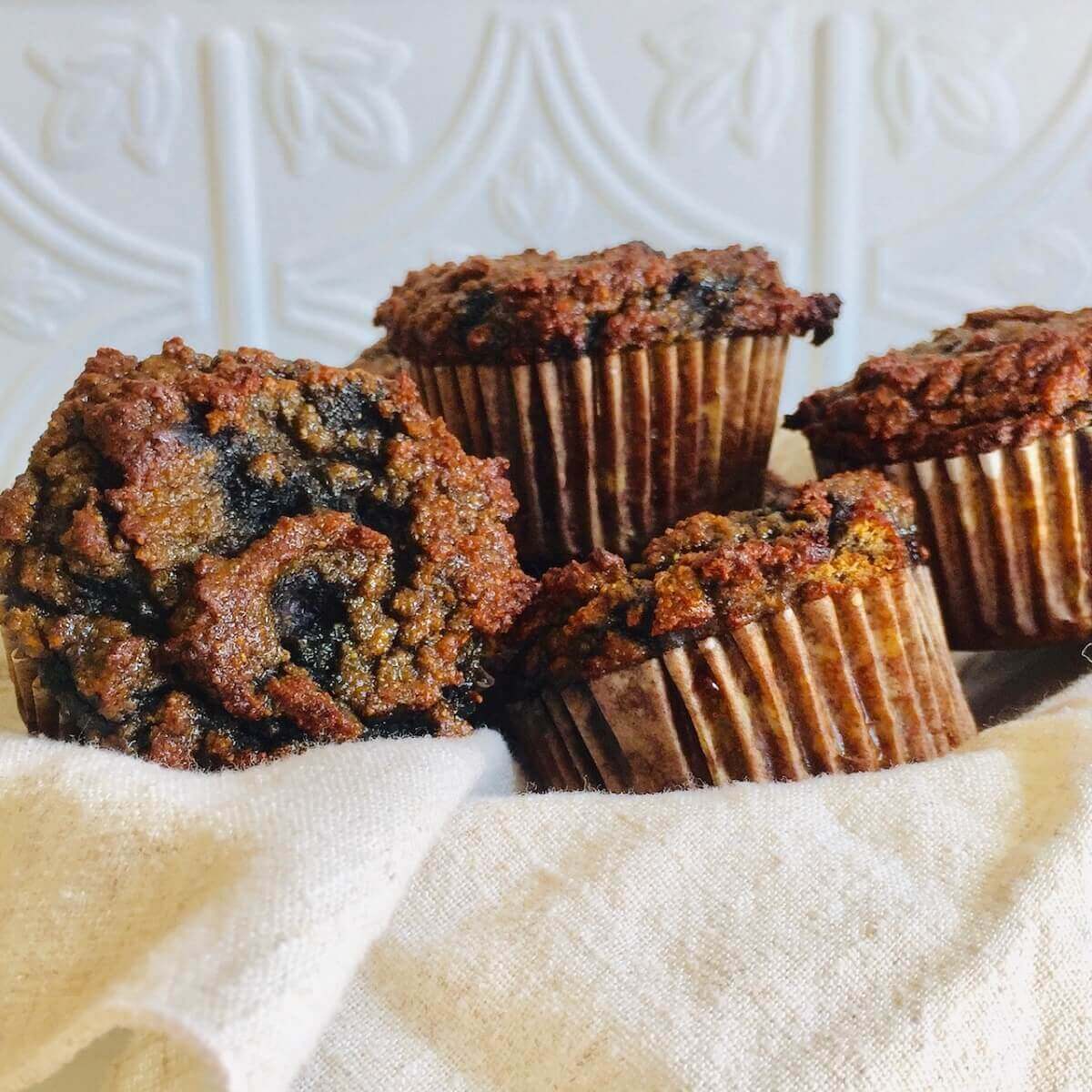 A basket filled with paleo blueberry banana muffins against a white tile background.