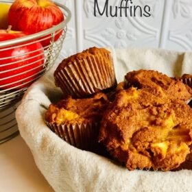 A basket of muffins next to some apples.