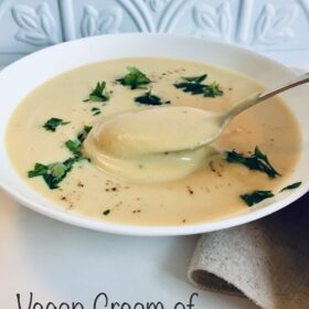 A bowl of cauliflower soup with a spoon lifting a bite and green parsley sprinkled on top.