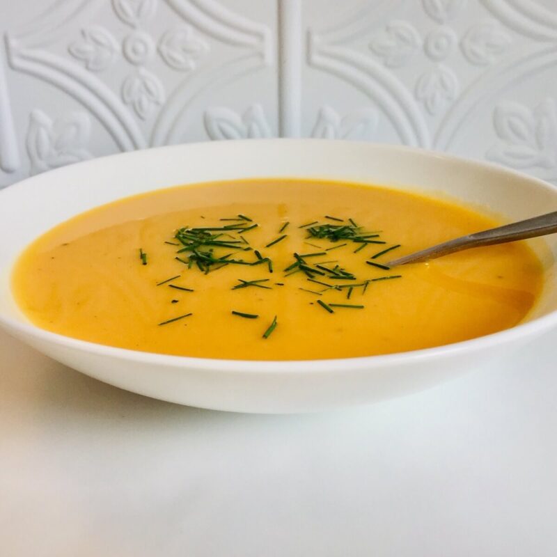 A white bowl of butternut squash soup with chives sprinkled on top.