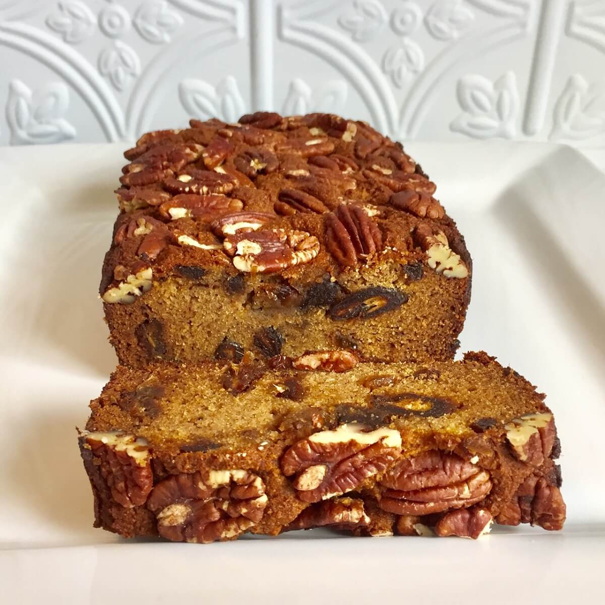 A slab of gluten free fruit cake on a white platter with a slice cut off.