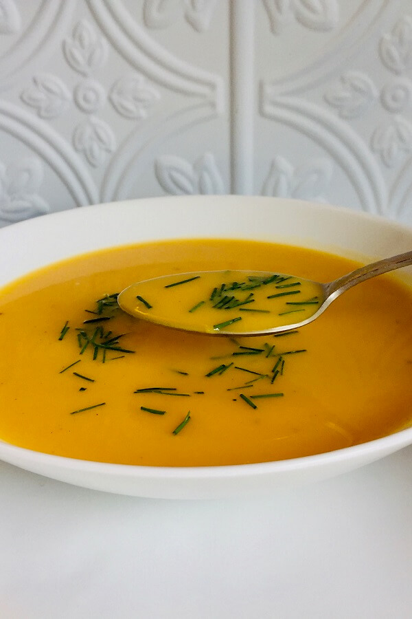 Paleo butternut squash soup with a spoon against a white tile background.