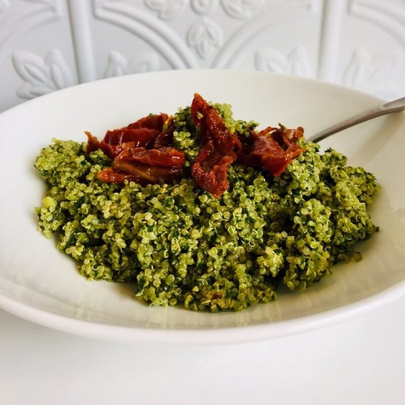Pesto quinoa in a white bowl with a few sun dried tomatoes on top.
