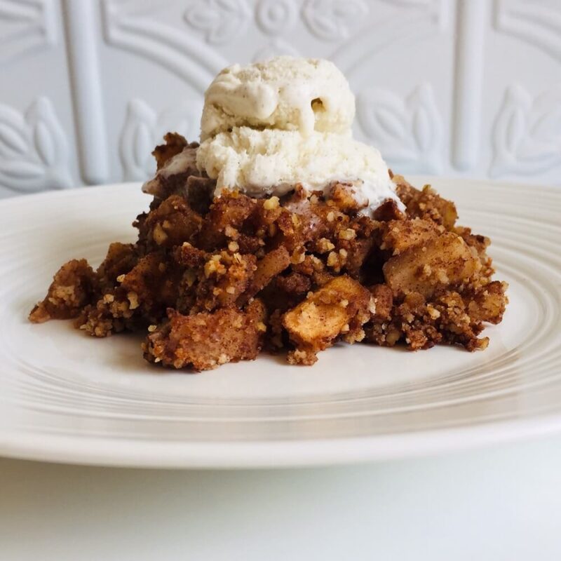 A pile of gluten-free vegan apple crumble with ice cream on a white plate.