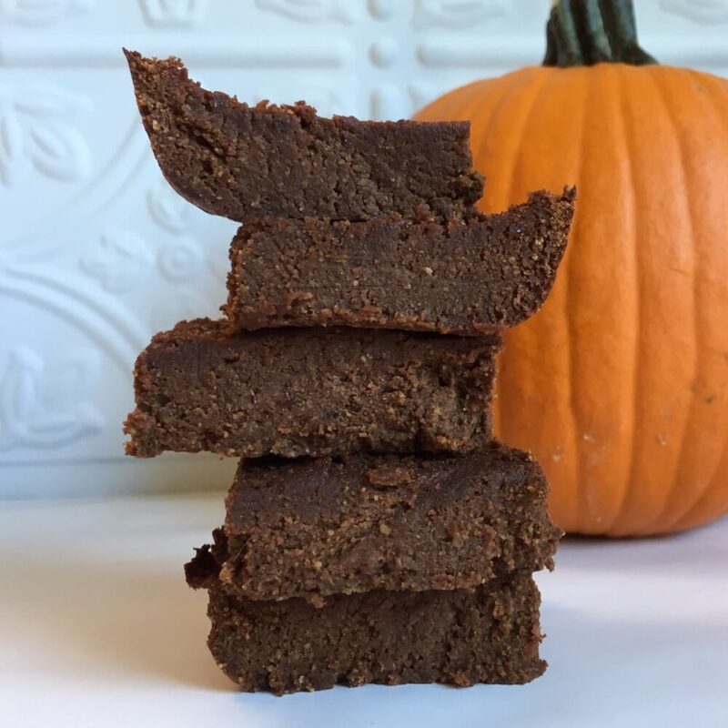 Pumpkin brownies piled next to a pumpkin against a white tile background.