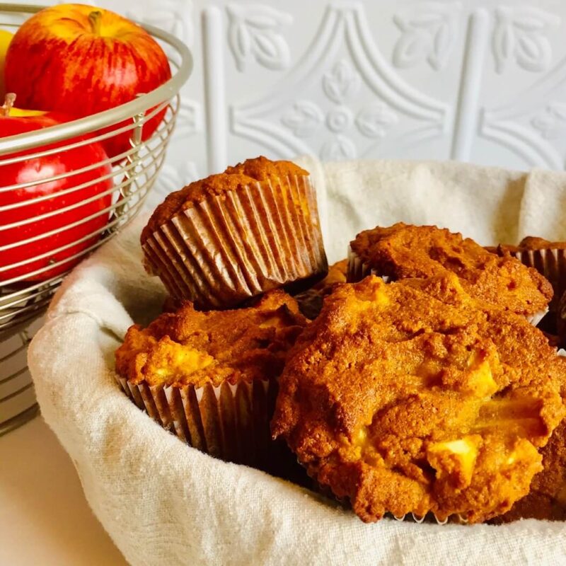 Muffins in a basket next to some apples.