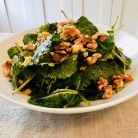 A white bowl filled with balsamic kale salad with walnuts sprinkled on top.