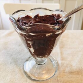Chocolate pudding in a glass dish with a metal spoon.