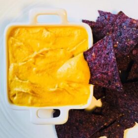 Dairy free nacho cheese sauce and blue corn chips on a plate.