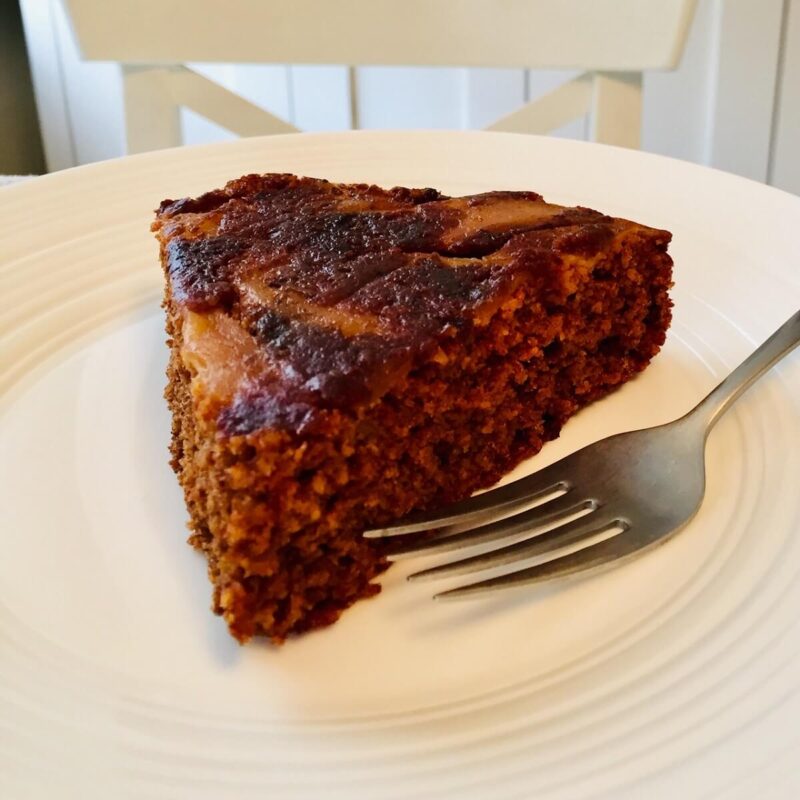 Close up of a slice of gluten free apple upside down cake on a white plate.