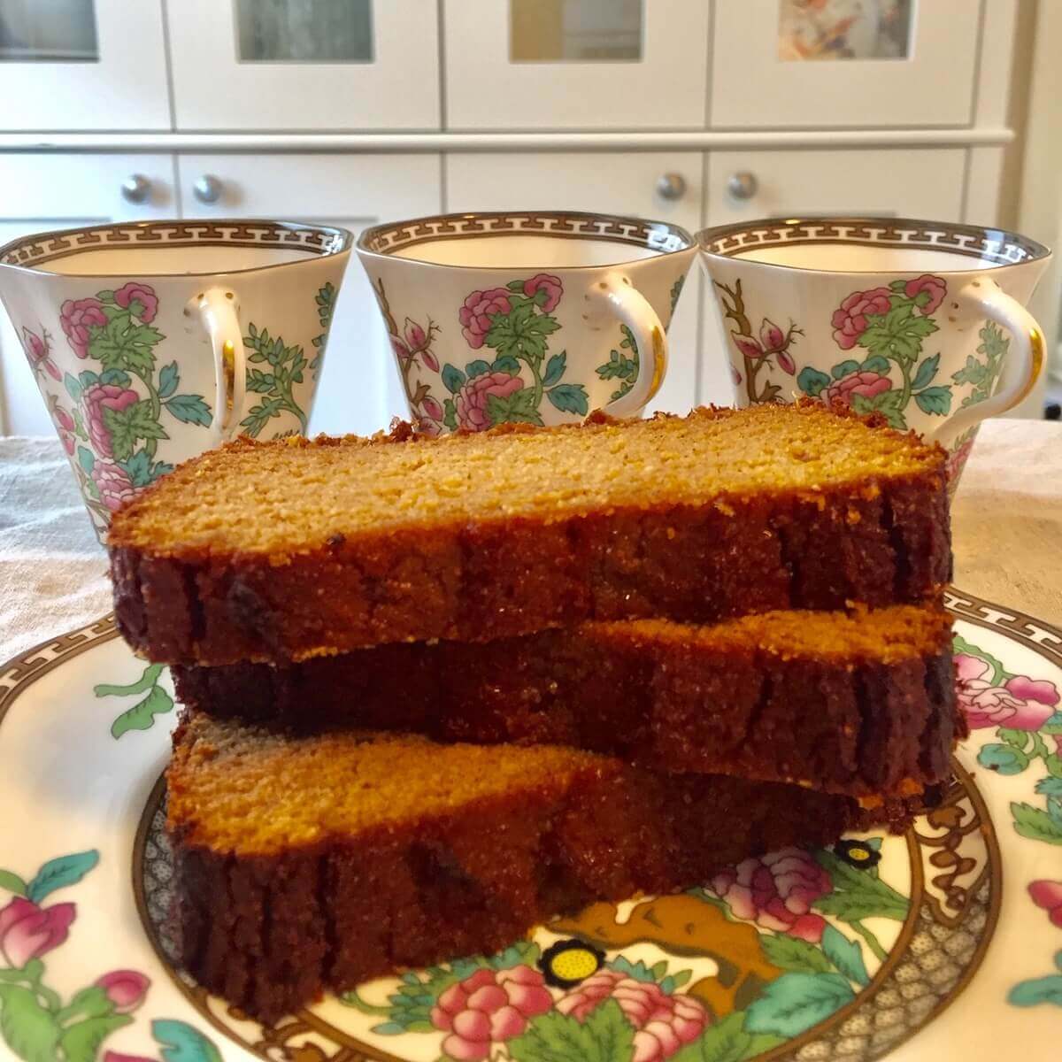 Slices of gluten free sweet potato bread stacked on a floral plate next to three cups.
