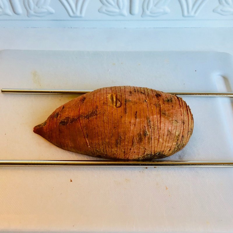 A sweet potato on a cutting board with a steel straw on either side.