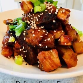 Tofu cubes in a red sauce in a white bowl.