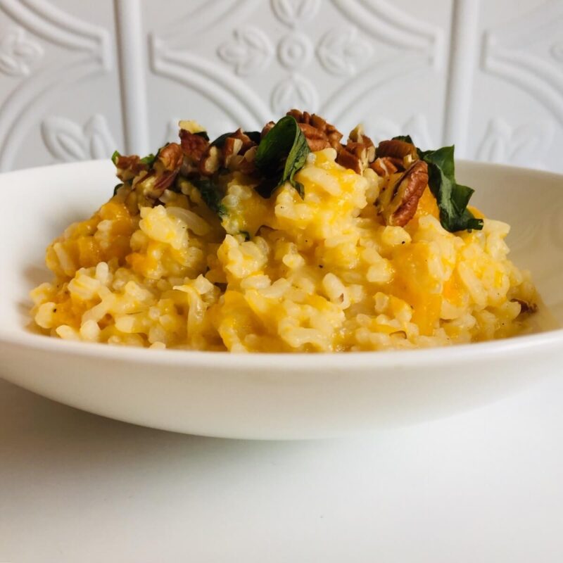 A white bowl filled with vegan butternut squash risotto against a white tile background.