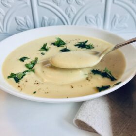 A bowl of vegan cream of cauliflower soup with a spoon lifting up a bite.