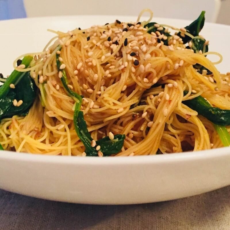 A white bowl filled with vegan rice noodles with sesame seeds sprinkled on top.