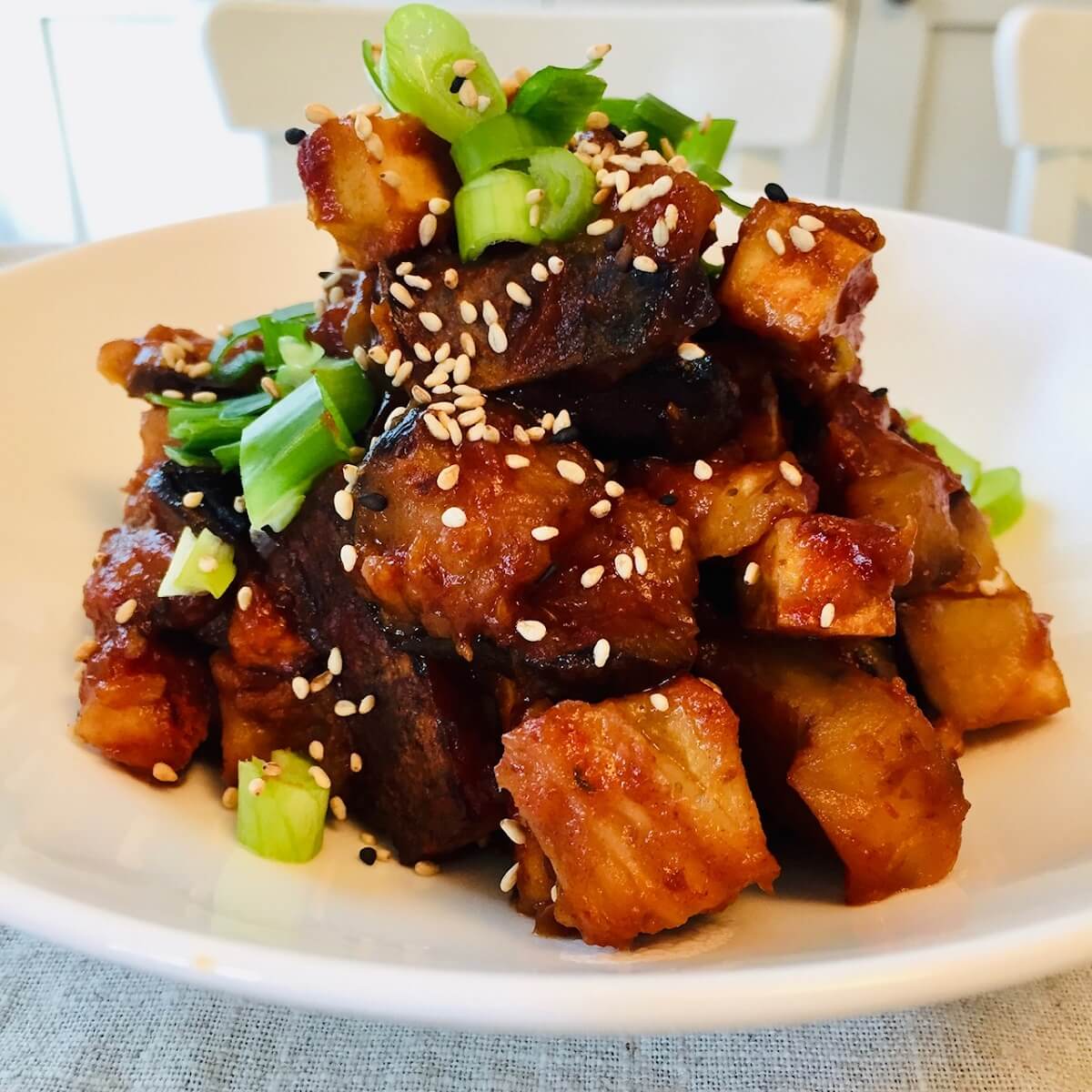 A white bowl filled with vegan sweet and sour tofu garnished with sesame seeds and green onions.