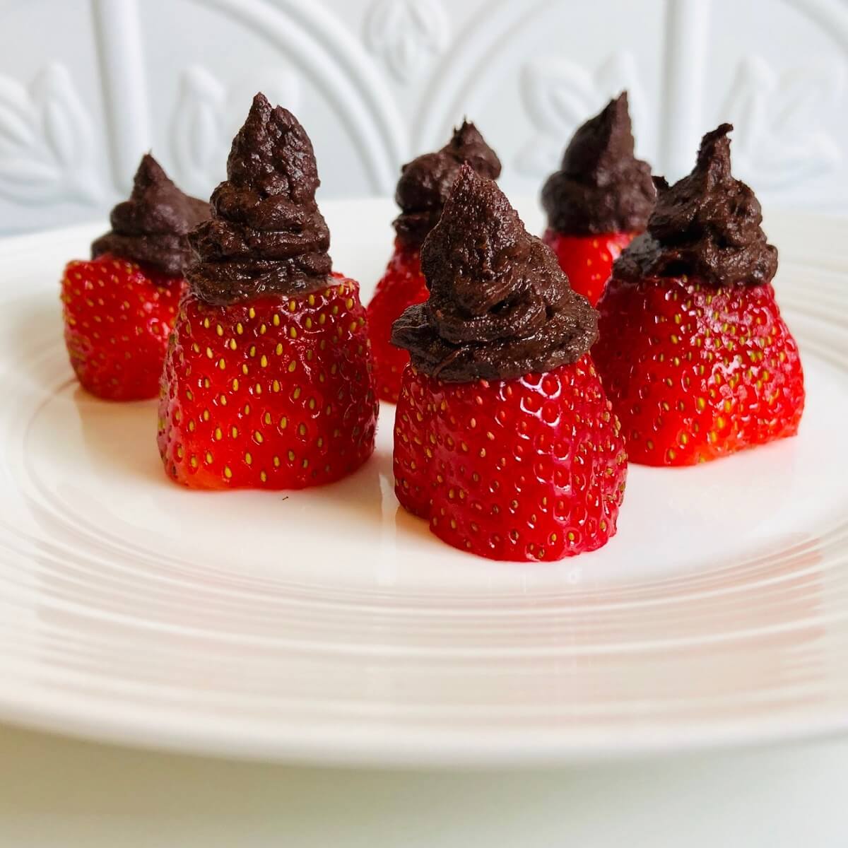 Six chocolate filled strawberries displayed on a white plate.