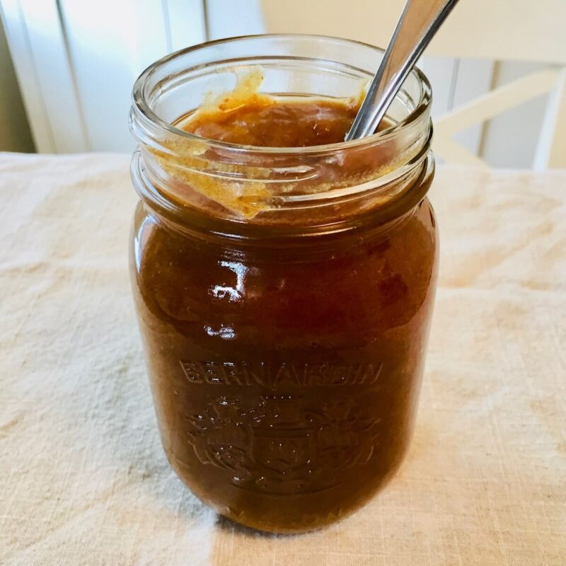 A glass mason jar filled with date paste with a spoon.