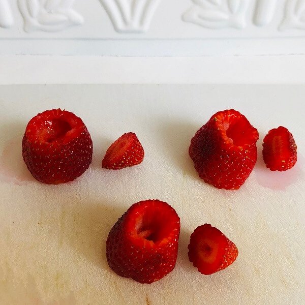 Hollowed out strawberries on a cutting board.