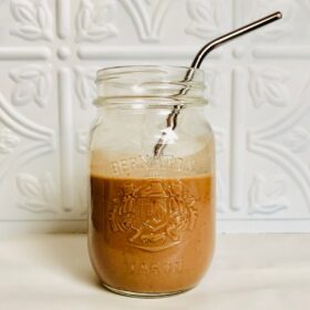 A glass mason jar halfway full of chocolate kefir smoothie with a stainless steel straw.