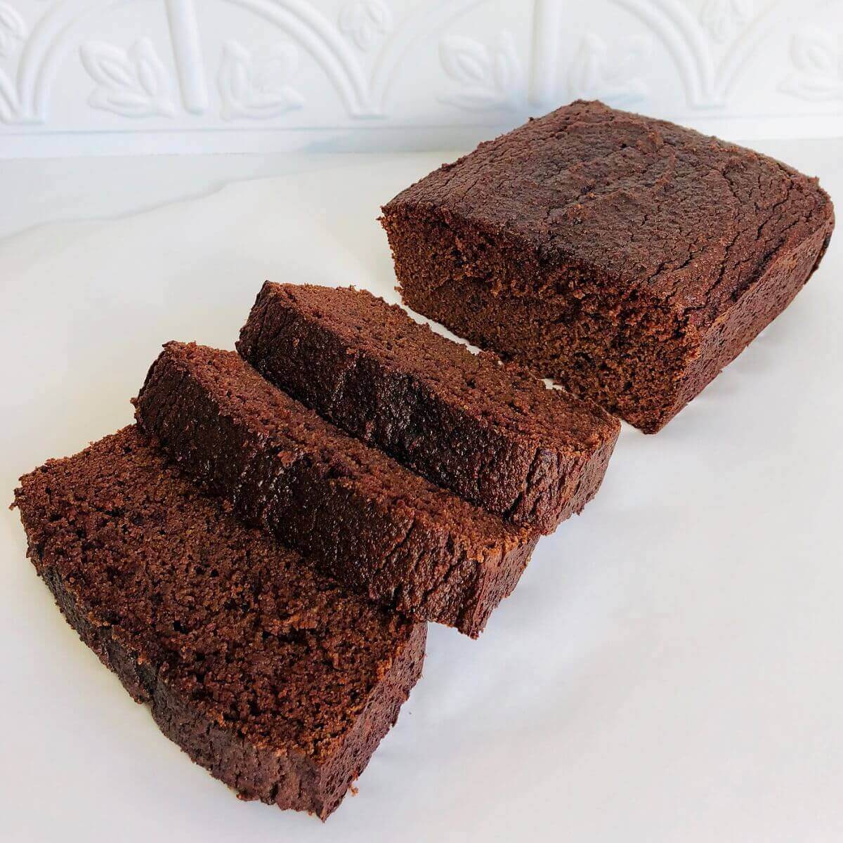Three slices of chocolate loaf cake next to a larger hunk against a white background.