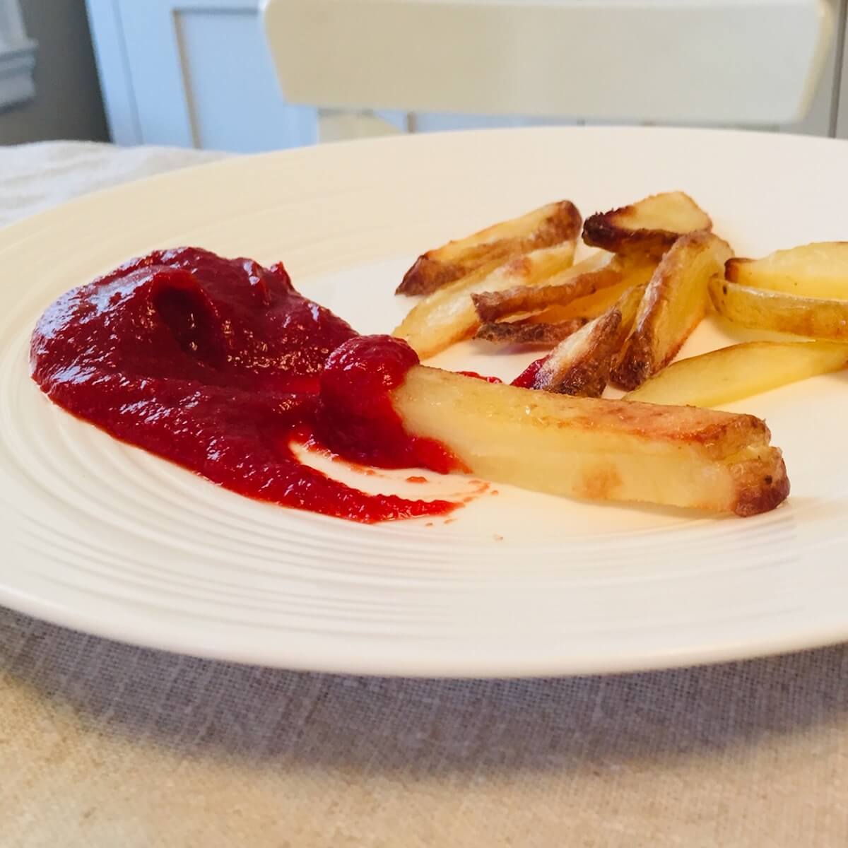 A white plate with french fries and some ketchup.