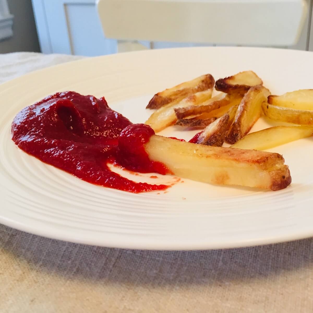 A white plate with French fries and some ketchup.