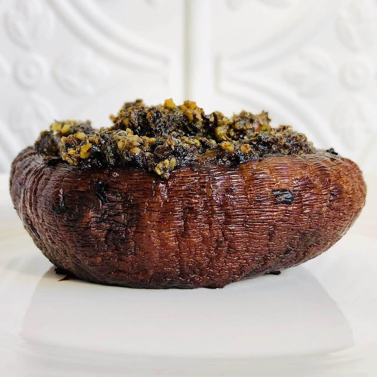 A single gluten-free, vegan stuffed portobello mushroom on a white plate against a white tile background.