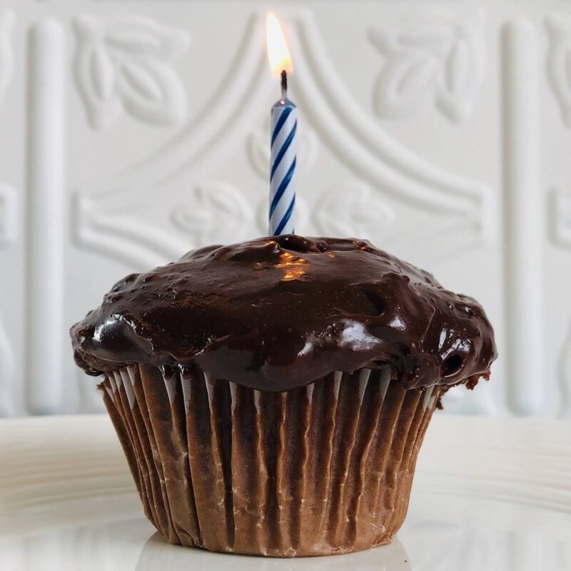 A cupcake topped with tahini frosting with a lit candle in it.