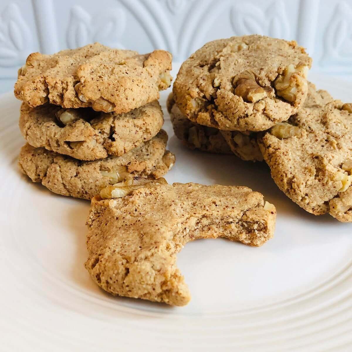 A white plate with a stack of vegan walnut cookies with a bite missing from one.