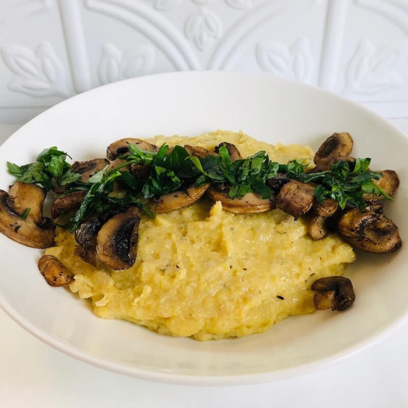A white bowl filled with creamy vegan baked polenta with some mushrooms on top.