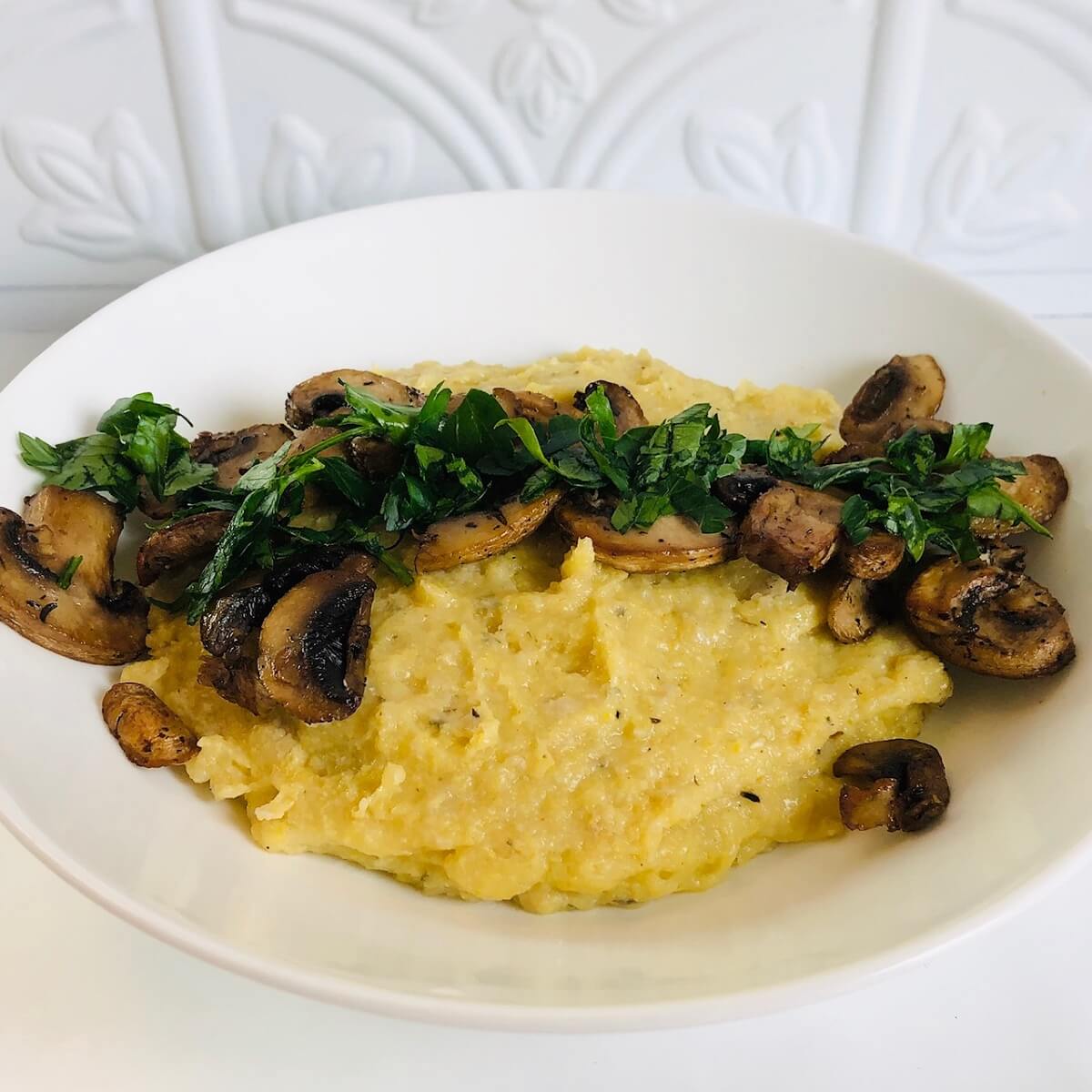 A white bowl filled with creamy vegan baked polenta with some mushrooms on top.