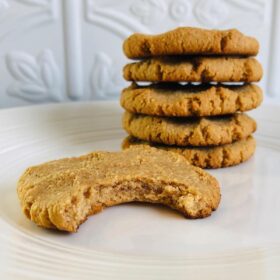 Five coconut flour peanut butter cookies on a white plate with a bite taken out of one.