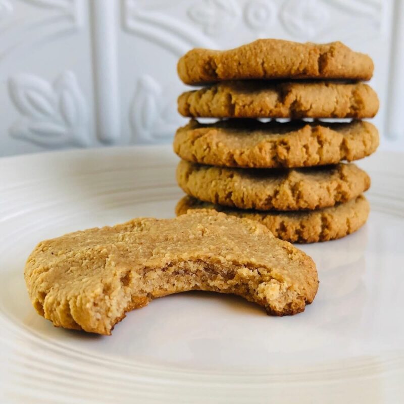 Five cookies stacked on a white plate with a bite taken out of one.