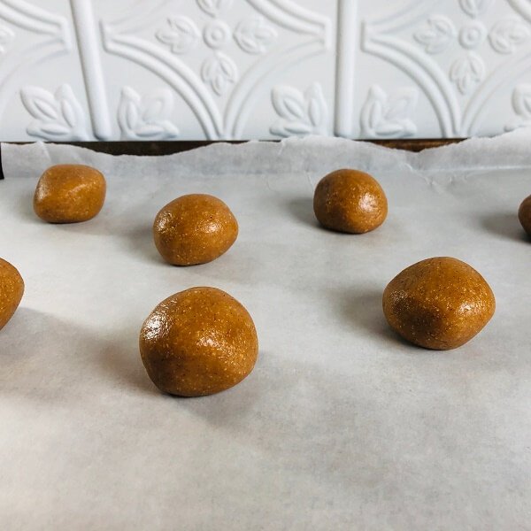 Raw balls of cookie dough on a sheet pan lined with paper.