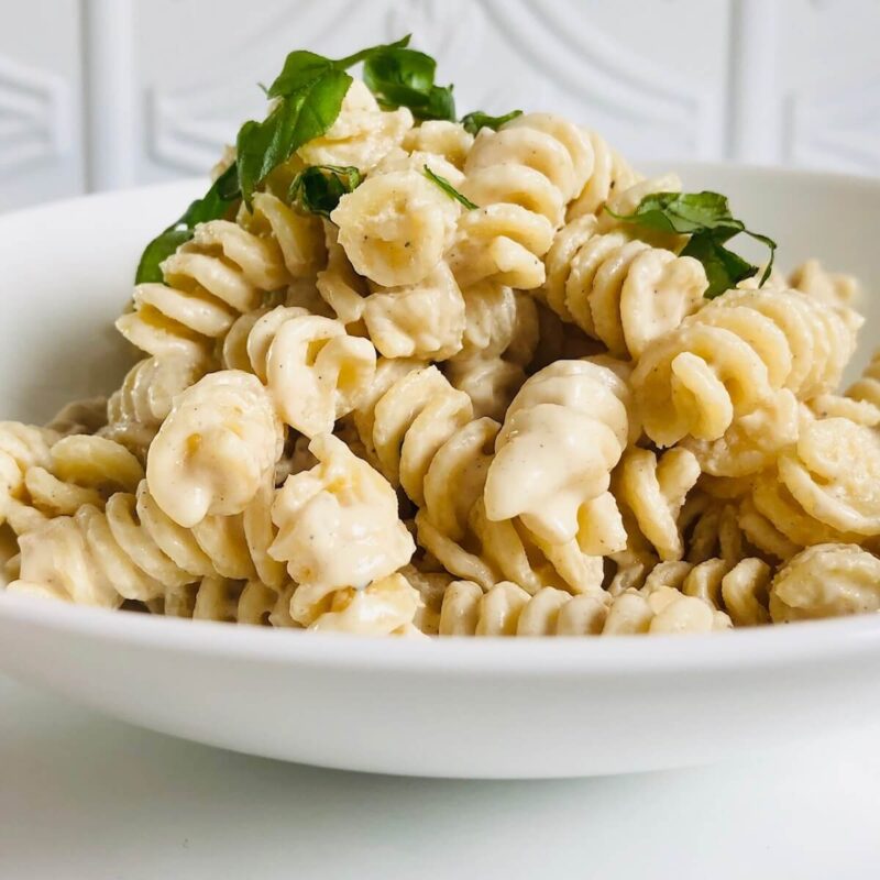 A white bowl filled with pasta in a creamy sauce.