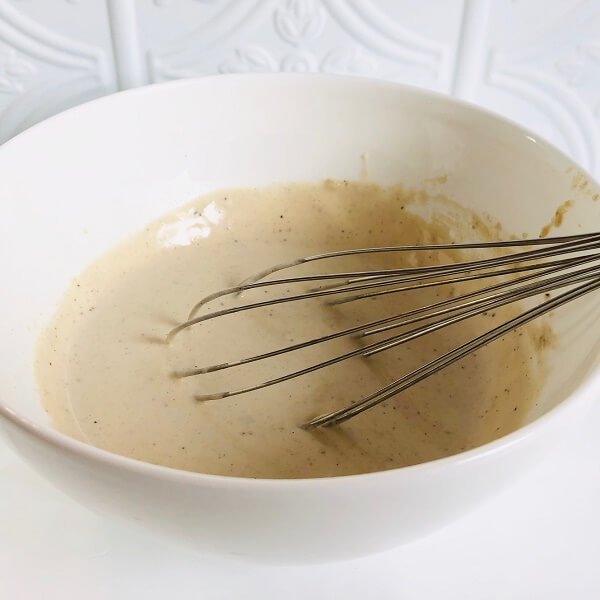 A bowl of creamy looking sauce with a whisk in it.