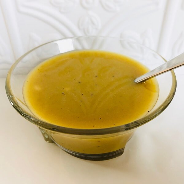 A glass bowl full of maple syrup salad dressing with a spoon in it.