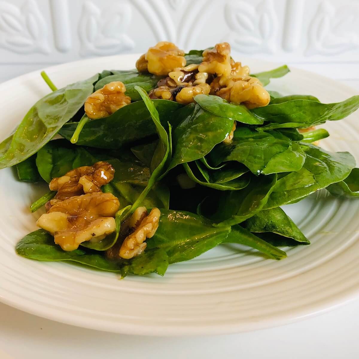 A white plate full of salad tossed with maple vinaigrette with walnuts sprinkled on top.