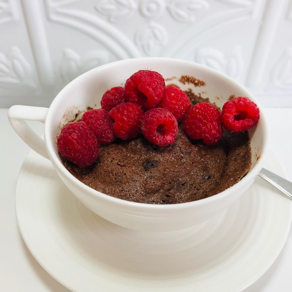 Paleo chocolate cake in a mug with raspberries on top.