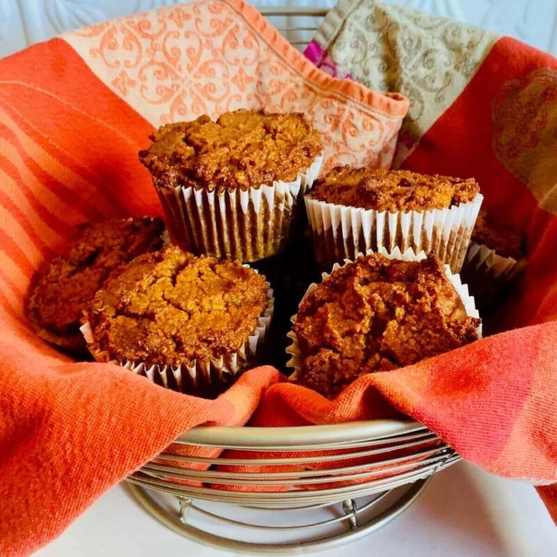A wire basket of muffins wrapped in an orange tea towel.