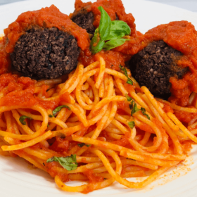 Pinterest image of plant-based meatballs with pasta in a red sauce.