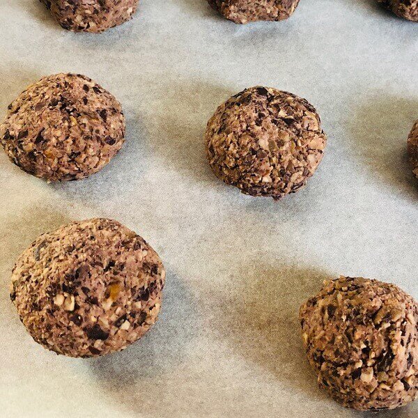 Raw meatballs on a parchment paper lined baking sheet.