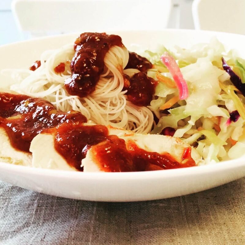 A bowl of noodles, chicken, and cabbage smothered in a red chili sauce.