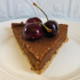 A slice of vegan cashew cheesecake with three cherries on top.