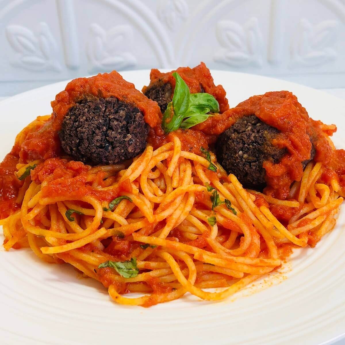 Three vegan meatballs on a plate of spaghetti with tomato sauce.