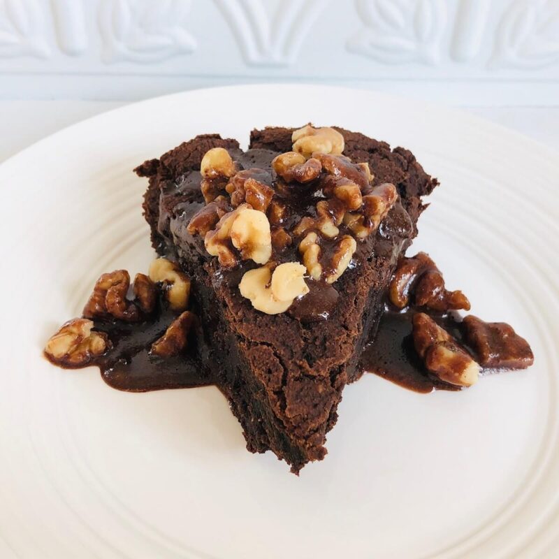 A slice of cake with walnuts and chocolate sauce on top.